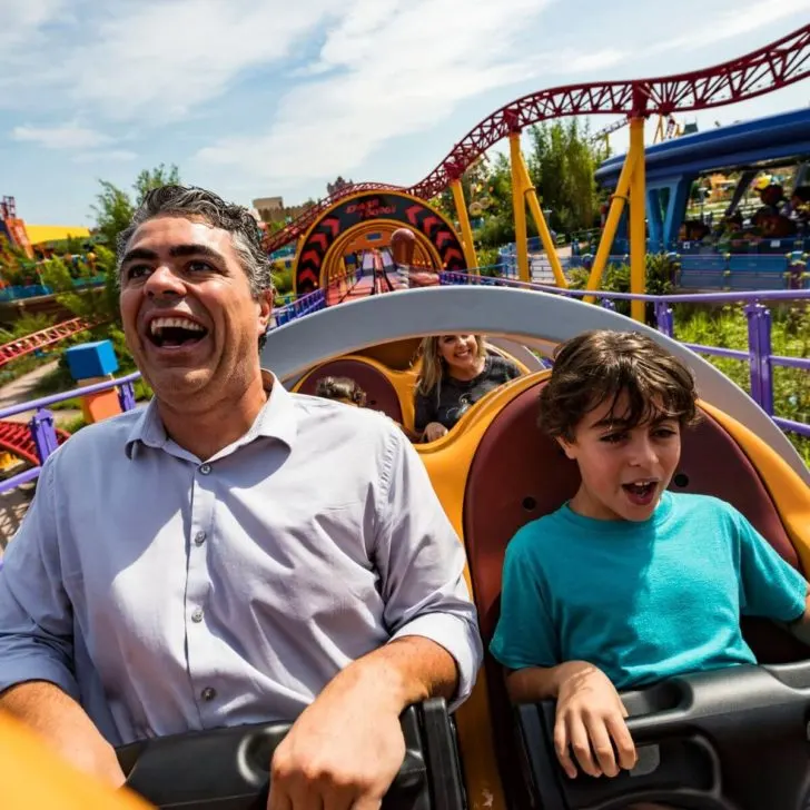 Photo of a man and young boy with brown hair sitting in the front seat of Slinky Dog Dash.
