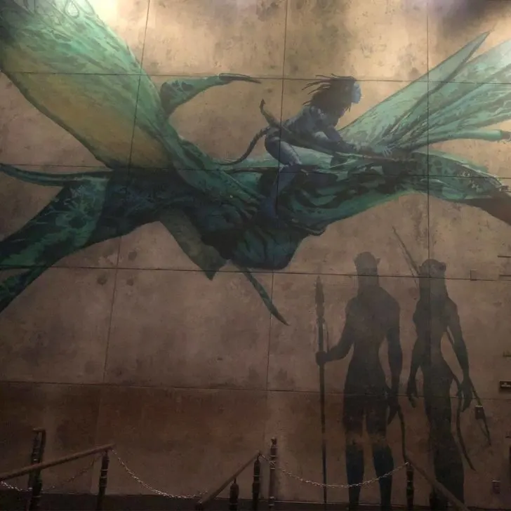 Photo of artwork depicting Na'vi, including one flying on an Ikran or banshee, along the queue for Avatar: Flight of Passage at Disney's Animal Kingdom.