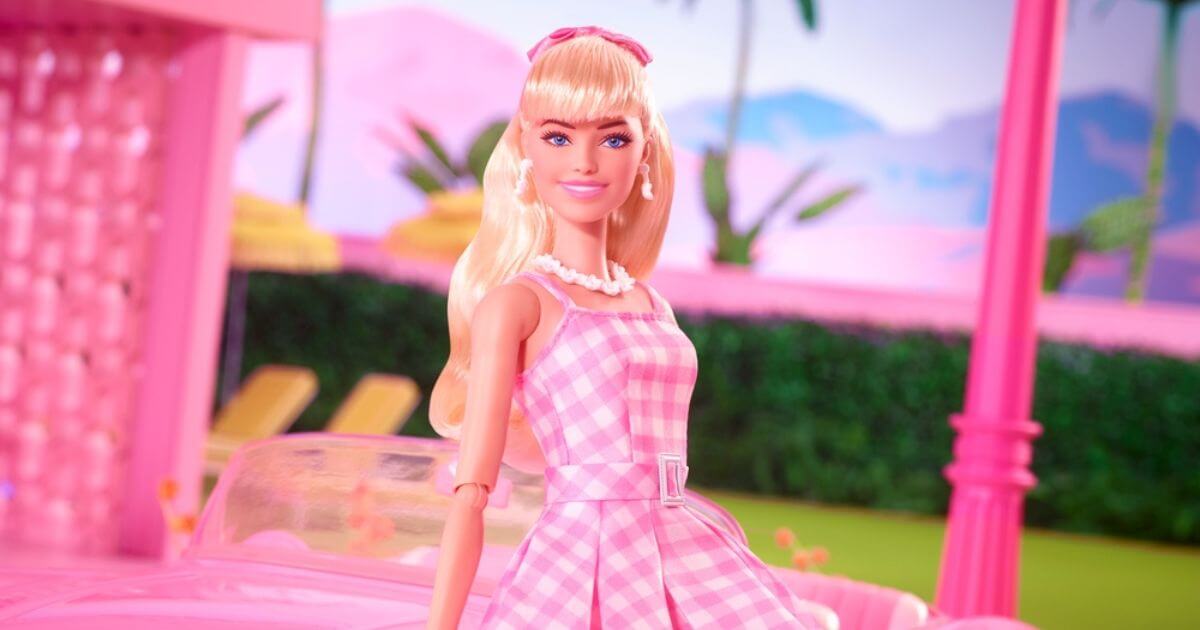Photo of a Barbie doll dressed in a pink gingham plaid dress, sitting on a pink convertible.
