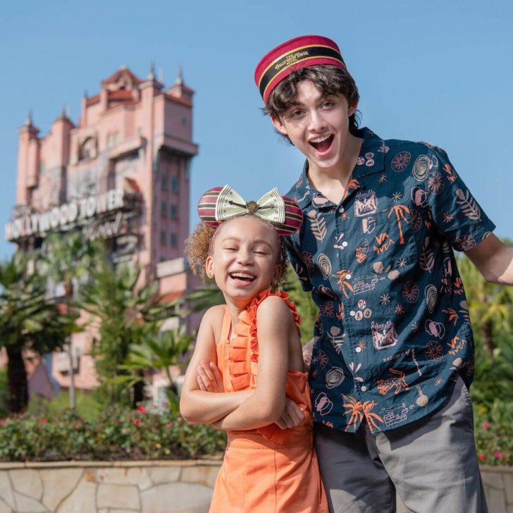 Actors Mykal-Michelle Harris and Felix Avitia (L-R) from Disney Channel’s “Raven’s Home” pose with Tower of Terror merchandise with the Hollywood Tower Hotel in the background.