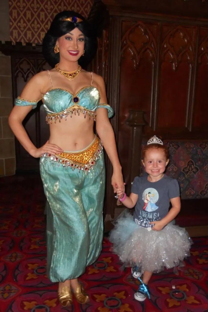 Photo of a young girl in a princess costume posing with Princess Jasmine at Cinderella's Royal Table restaurant.