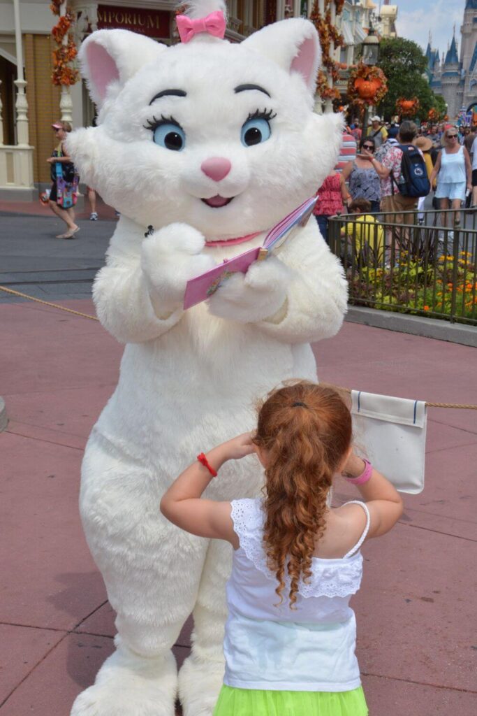 Photo of a young girl watching Marie from Aristocats sign an autograph book.