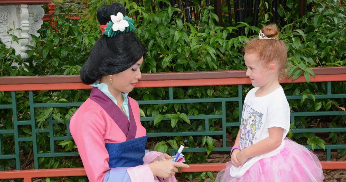Photo of a young girl chatting with Mulan as she signs an autograph at Epcot's China pavilion.