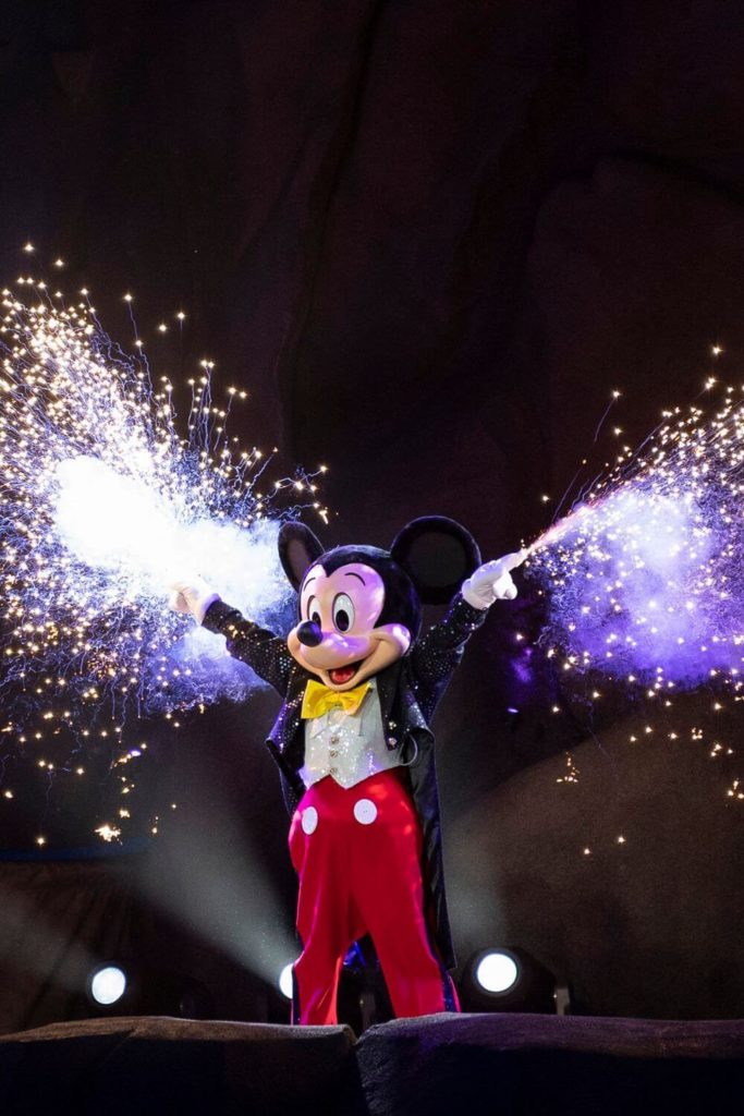 Photo of Mickey Mouse in a tuxedo with fireworks bursting from both hands during the nighttime show, Fantasmic!
