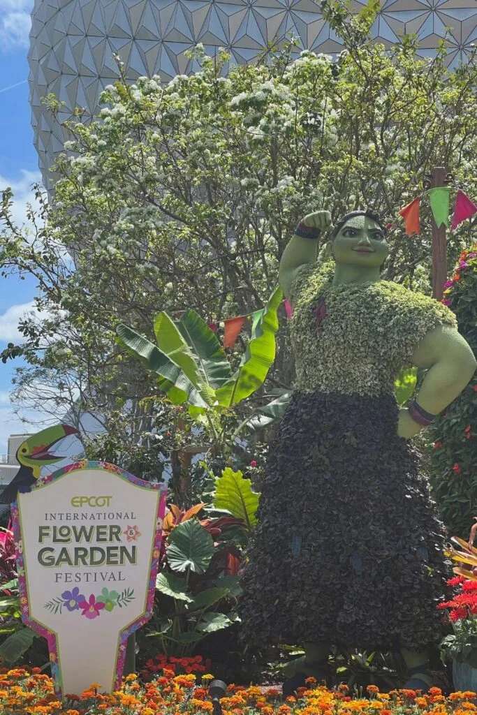Photo of a topiary of Luisa from Encanto next to a sign for the Epcot International Flower & Garden Festival.
