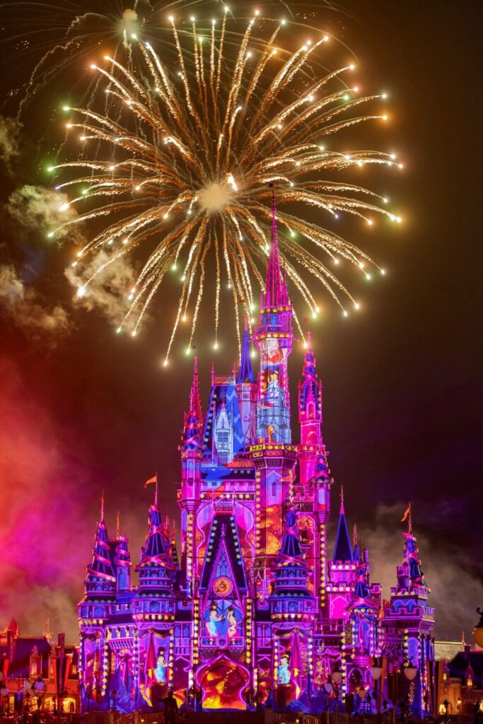 Photo of Cinderella's Castle lit up with a projection show while fireworks explode behind it.