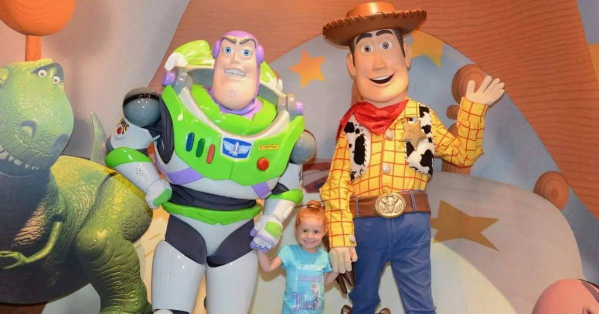 Photo of a toddler girl posing in between Buzz Lightyear (left) and Woody (right).