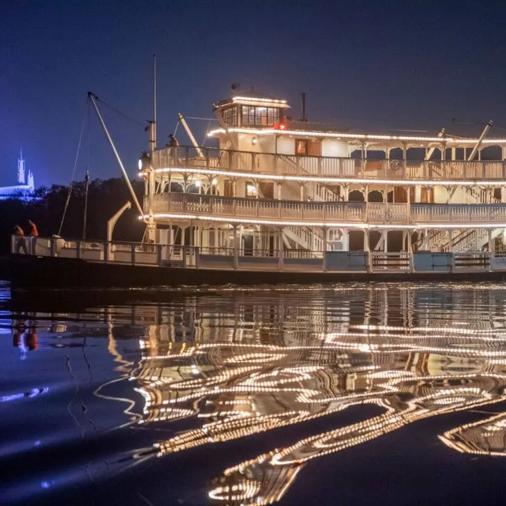 Photo of the Liberty Square riverboat at night, reflecting in the water.