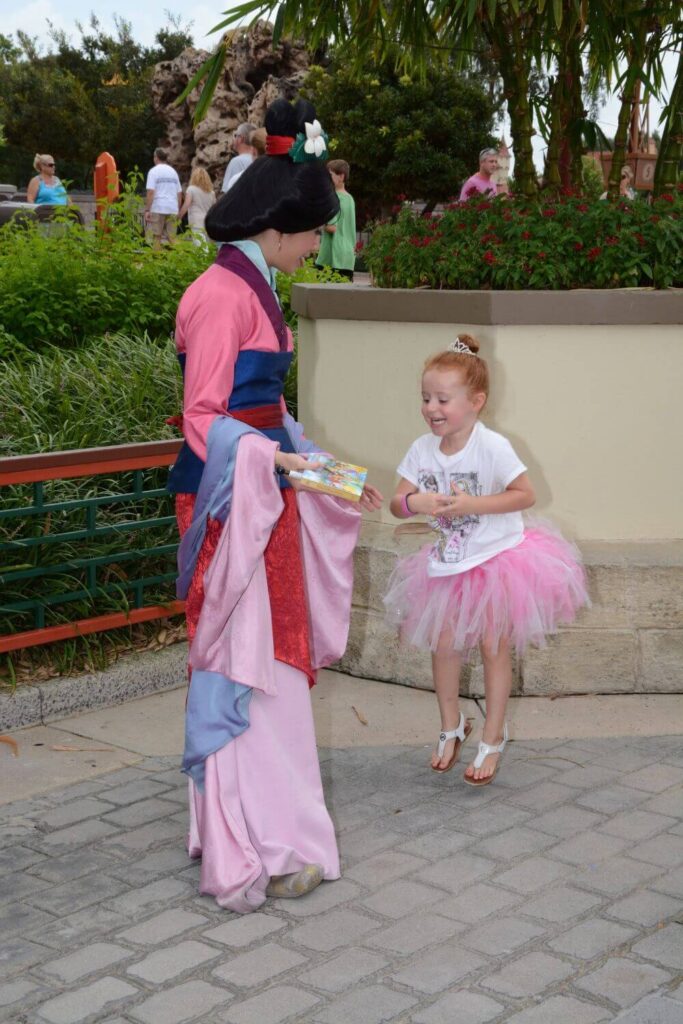 Photo of a young girl in a pink tutu jumping in the air as she greets Mulan at the China pavilion in Epcot.