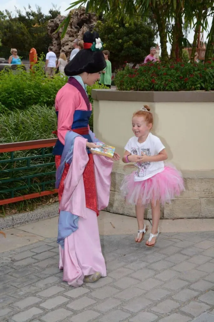 Photo of a young girl in a pink tutu jumping in the air as she greets Mulan at the China pavilion in Epcot.