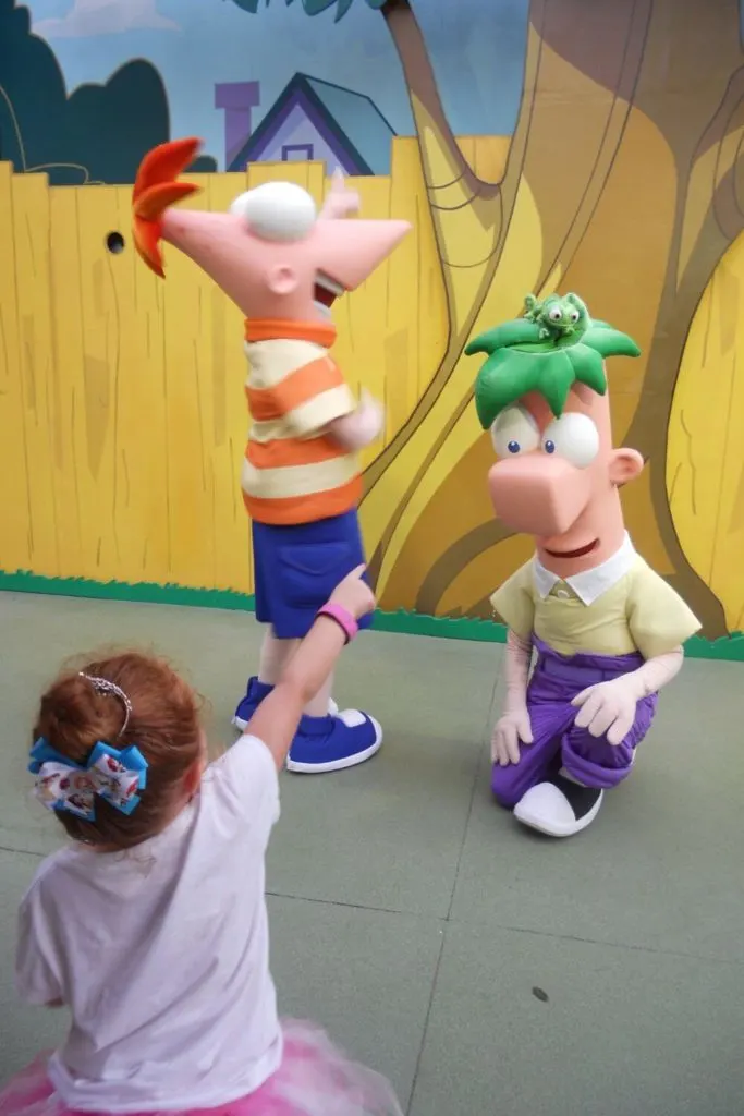 Photo of a young girl pointing at her stuffed animal on top of Ferb's head while Phineas laughs.