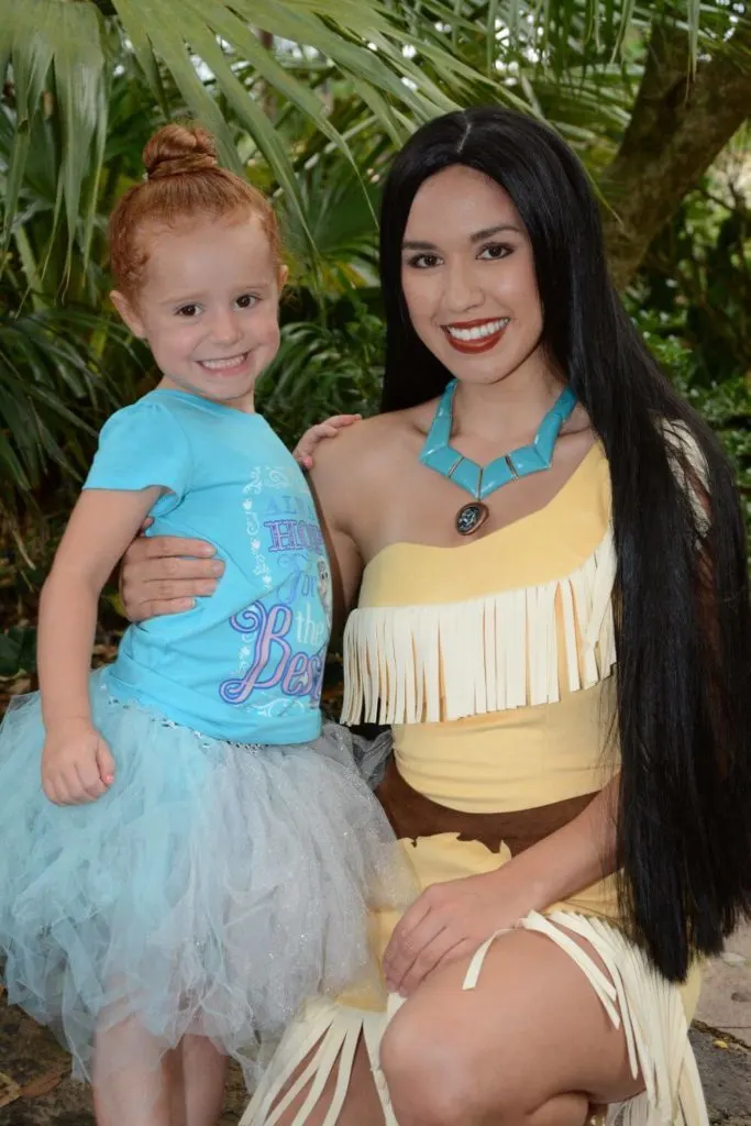 Photo of a toddler in a Frozen shirt and blue tutu while posing with Pocahontas.