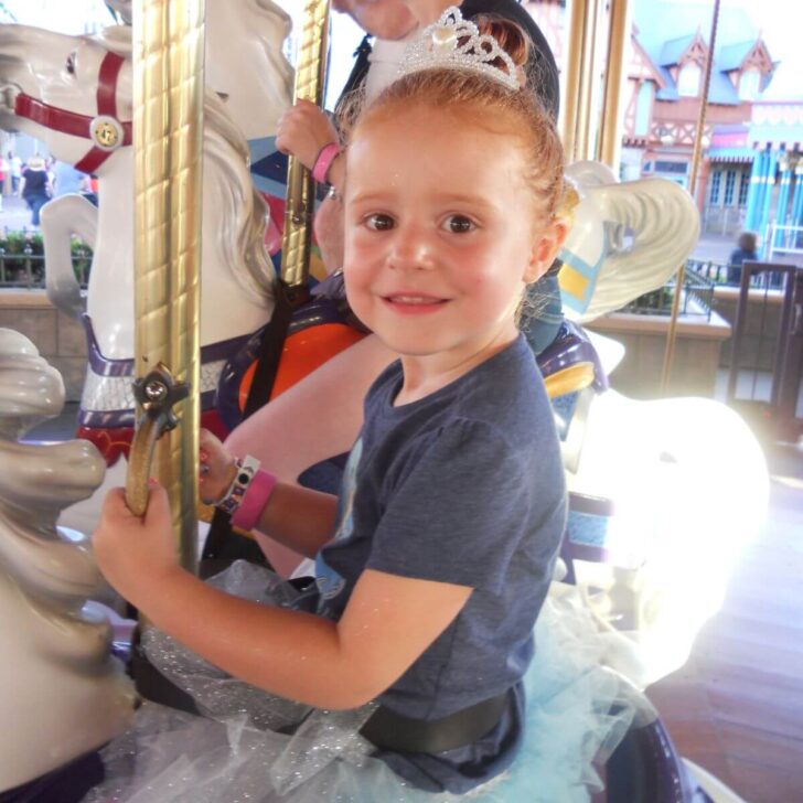 Photo of a young girl wearing a tiara and a tutu while riding the carousel at Magic Kingdom.