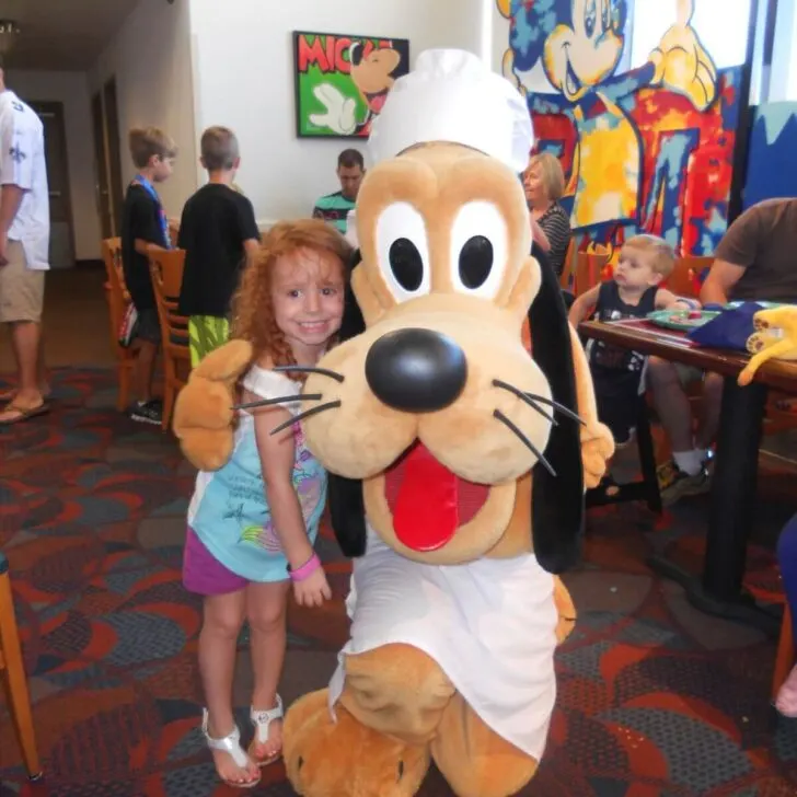 Photo of a young girl posing with Pluto at Chef Mickey's restaurant.
