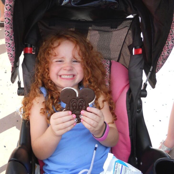 Photo of a young girl in a stroller posing with a Mickey Mouse ice cream sandwich.