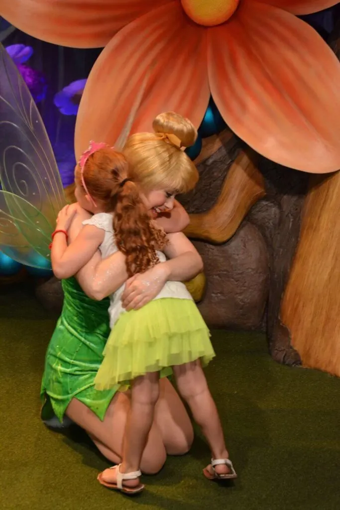Photo of a toddler wearing a green tutu hugging Tinkerbell at Magic Kingdom.