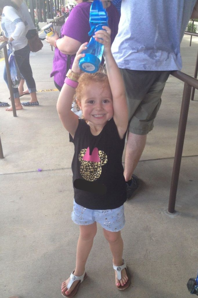 Photo of a toddler at Animal Kingdom wearing a shirt with a leopard print Minnie Mouse head and carrying a mister fan.