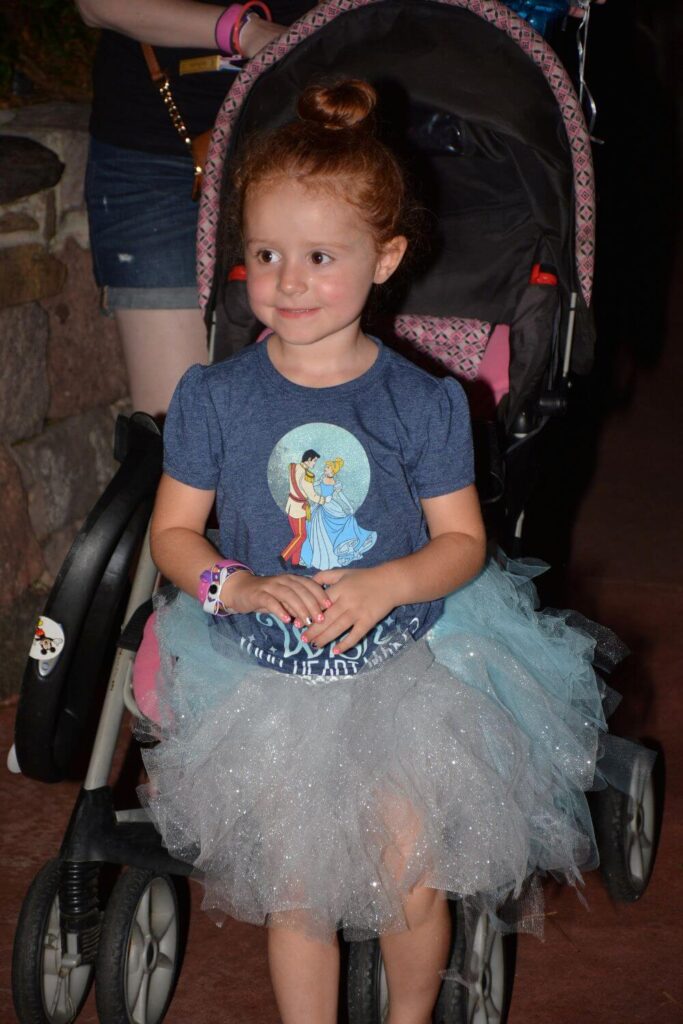 Photo of a young girl dressed as Cinderella, standing in front of a stroller.