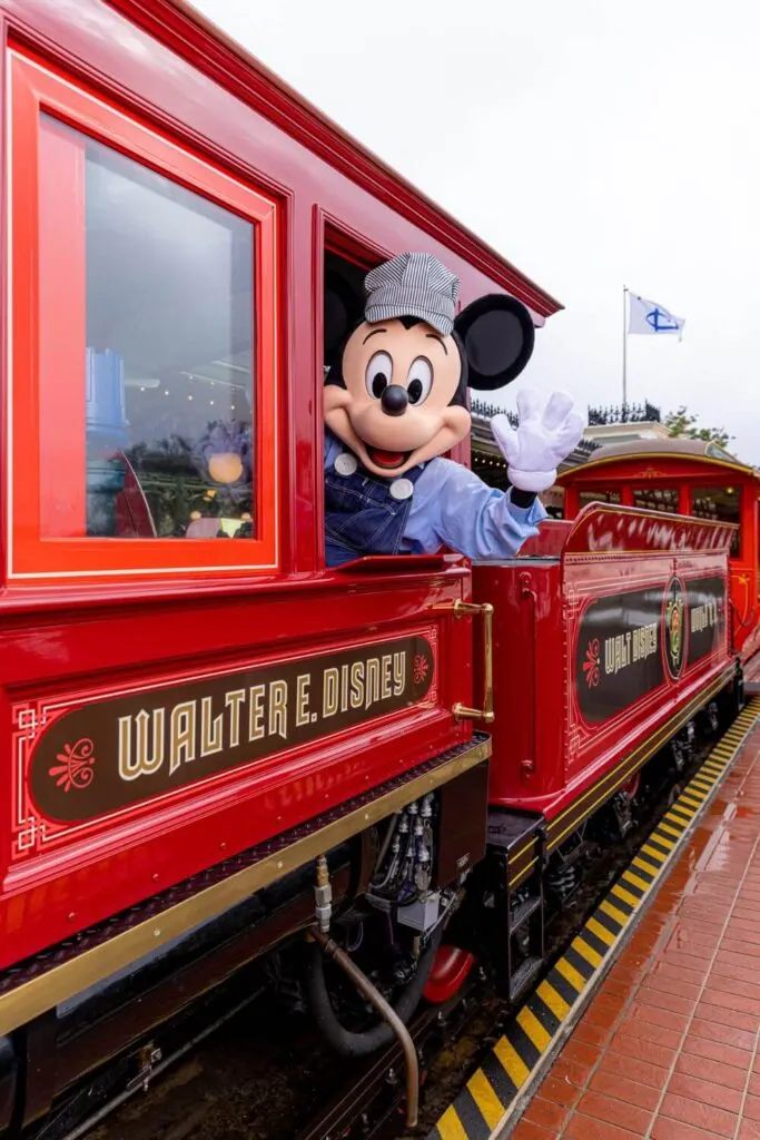 Photo of Mickey Mouse in a train engineer uniform, posing with the Walt Disney World Railroad train.