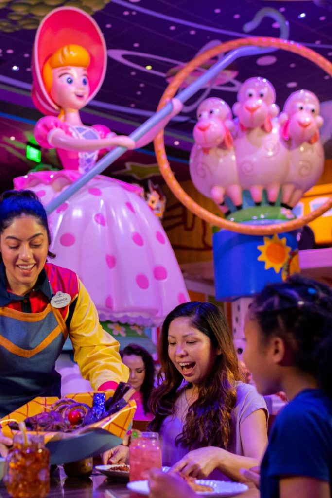 Photo of a server placing down a dish at a table with a mom and young girl at Roundup Rodeo BBQ with a massive Bo Peep statue in the background.