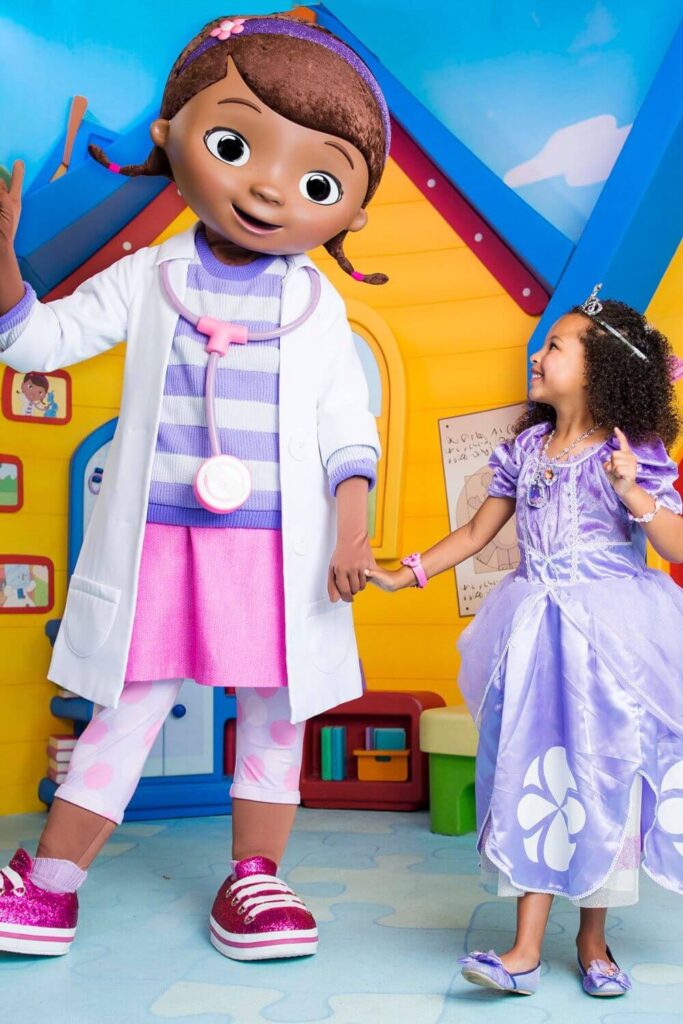 Photo of Doc McStuffins posing for a photo with a young girl in a purple princess dress.