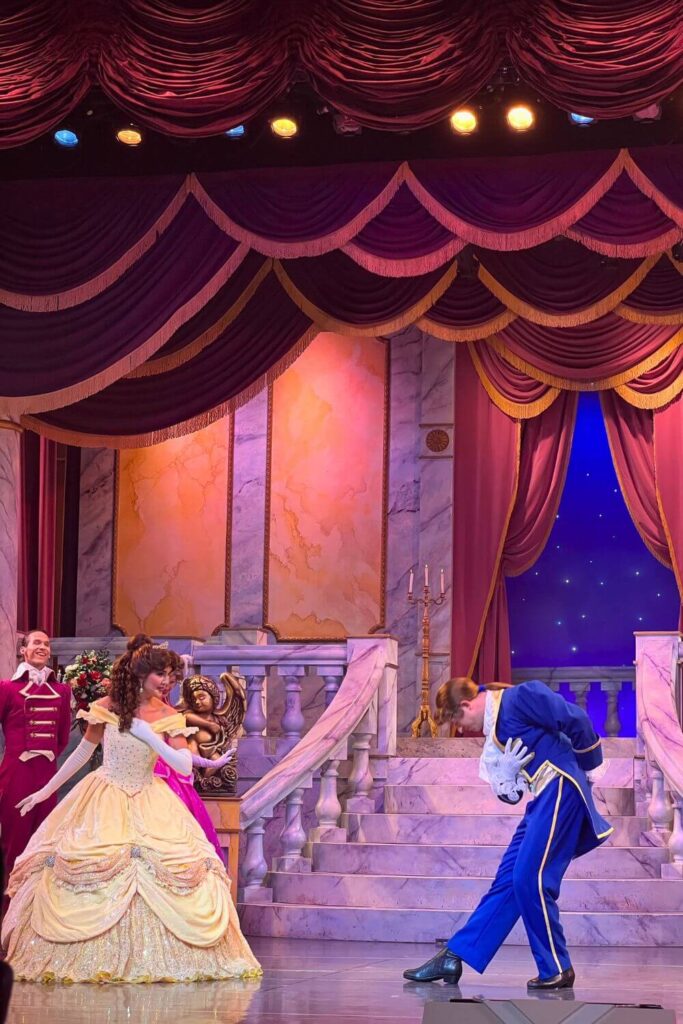 Photo of a scene from the Beauty & the Beast Live on Stage show, with Belle in her iconic yellow gown and the Beast transformed into a handsome prince in a fancy suit.