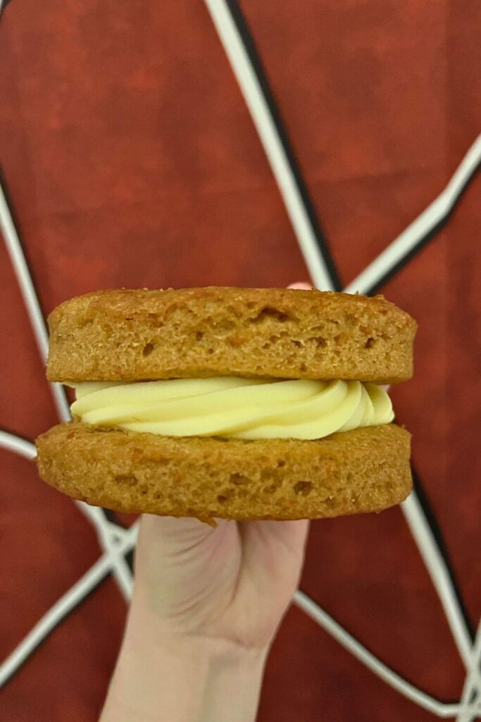 Photo of a massive carrot cake cookie - 2 round carrot cake slabs sandwiching a thick layer of cream cheese frosting.