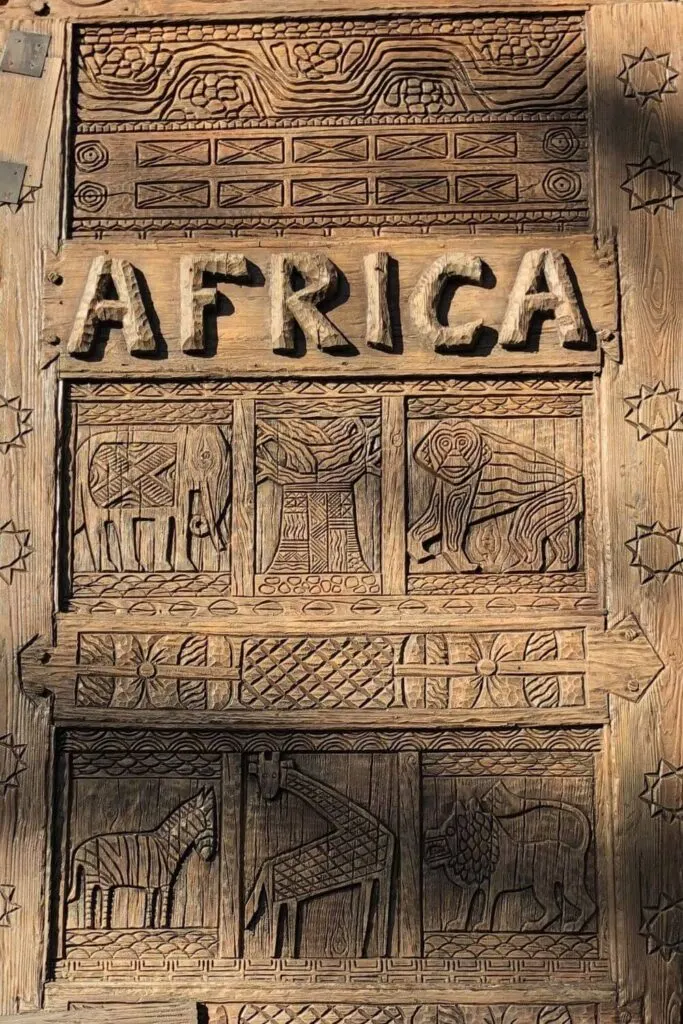 Closeup of the intricately carved wooden gate at the entrance to the Africa section of Disney's Animal Kingdom, with patterns, animals, and "Africa" carved into the gate.