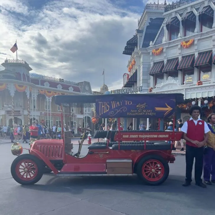 Photo of an old-fashioned car with signage pointing toward the MNSSHP entrance with cast members directing guests.