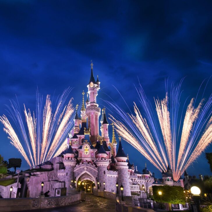 Photo of the castle at Disneyland Paris at night, with fireworks bursting behind it.