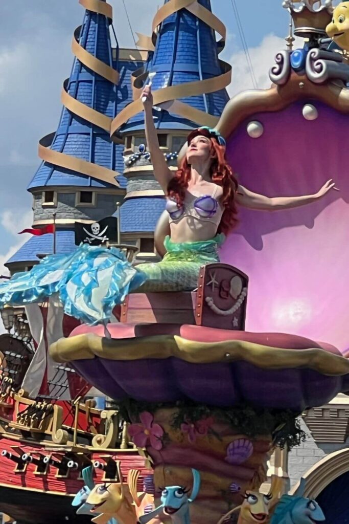 Photo of Ariel sitting on a parade float, holding up a dinglehopper while admiring it.