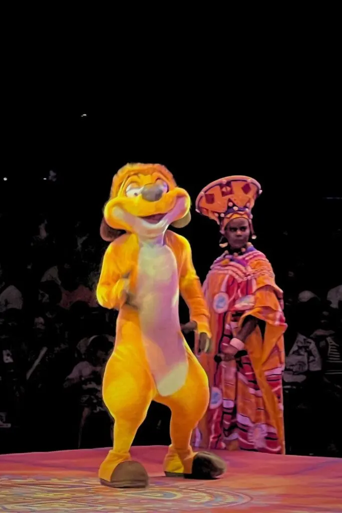 Photo of Timon and a female singer wearing a traditional African-style outfit while performing in Festival of the Lion King.