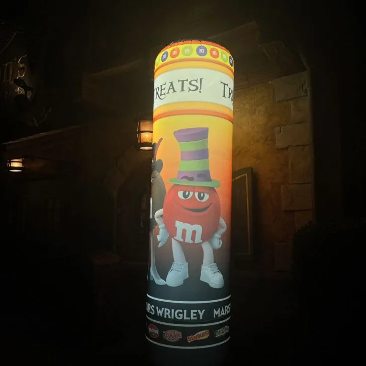 Photo of a pillar with an M&M character in a costume, logos for various Mars Wrigley candies, and text that says "Treats!"