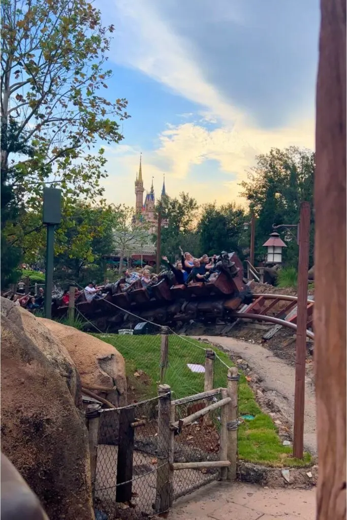 Photo of a mine train car with riders riding by on Seven Dwarfs Mine Train with Cinderella's Castle in the background.