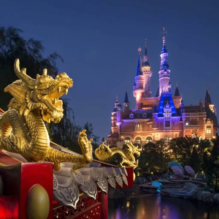 Photo of the Shanghai Disneyland castle at night with an elaborate Chinese-style structure in the foreground that features golden dragons.