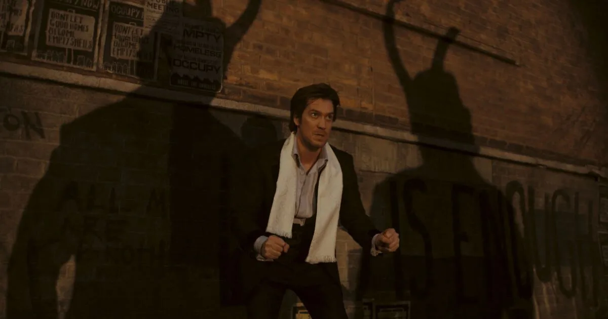Photo still of Rafael Casal as Brad Wolfe in Marvel Studios' LOKI, Season 2, Episode 2. He is standing in a defensive pose, ready to fight. Two shadows appear on the wall behind him with the trademark Loki horns.