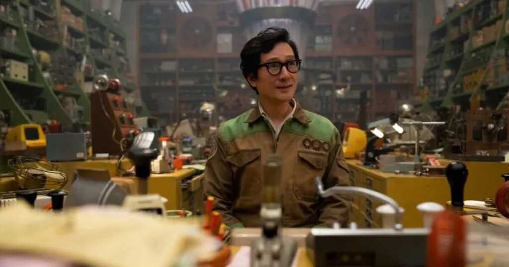 Photo still featuring Ke Huy Quan as O.B. (aka Ouroboros) in Marvel Studios' LOKI, Season 2, Episode 1. He is sitting behind a desk with tons of electronics and gadgets cluttered around him.