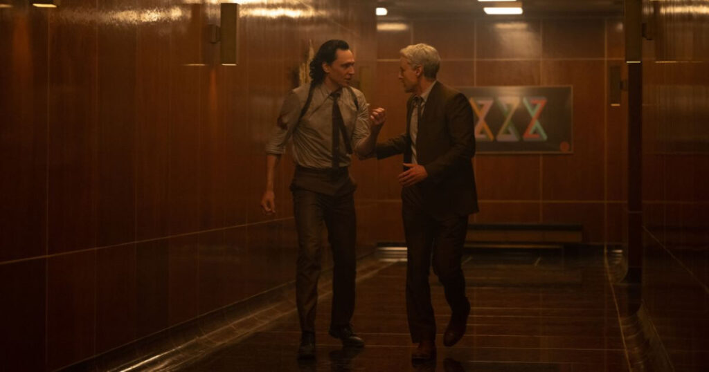 Photo still featuring (L-R): Tom Hiddleston as Loki and Owen Wilson as Mobius in Marvel Studios' LOKI, Season 2, Episode 1. The two are excitedly walking down a hall inside the TVA.