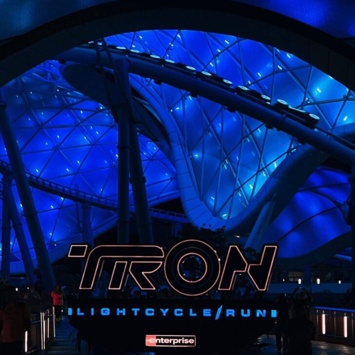Photo of the entrance to Tron Lightcycle Run at Disney World at night, with a line of cars whizzing by in the background.