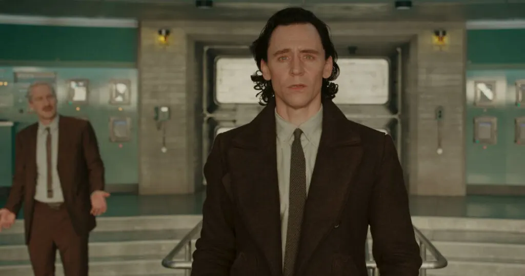 Photo still of Tom Hiddleston as Loki in Marvel Studios' LOKI, Season 2, episode 4, with Owen Wilson as Mobius in the background.
