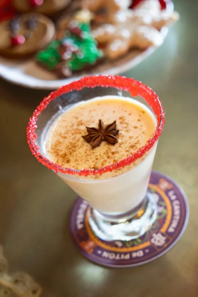 Photo of a glass of coquito with a plate of cookies in the background.