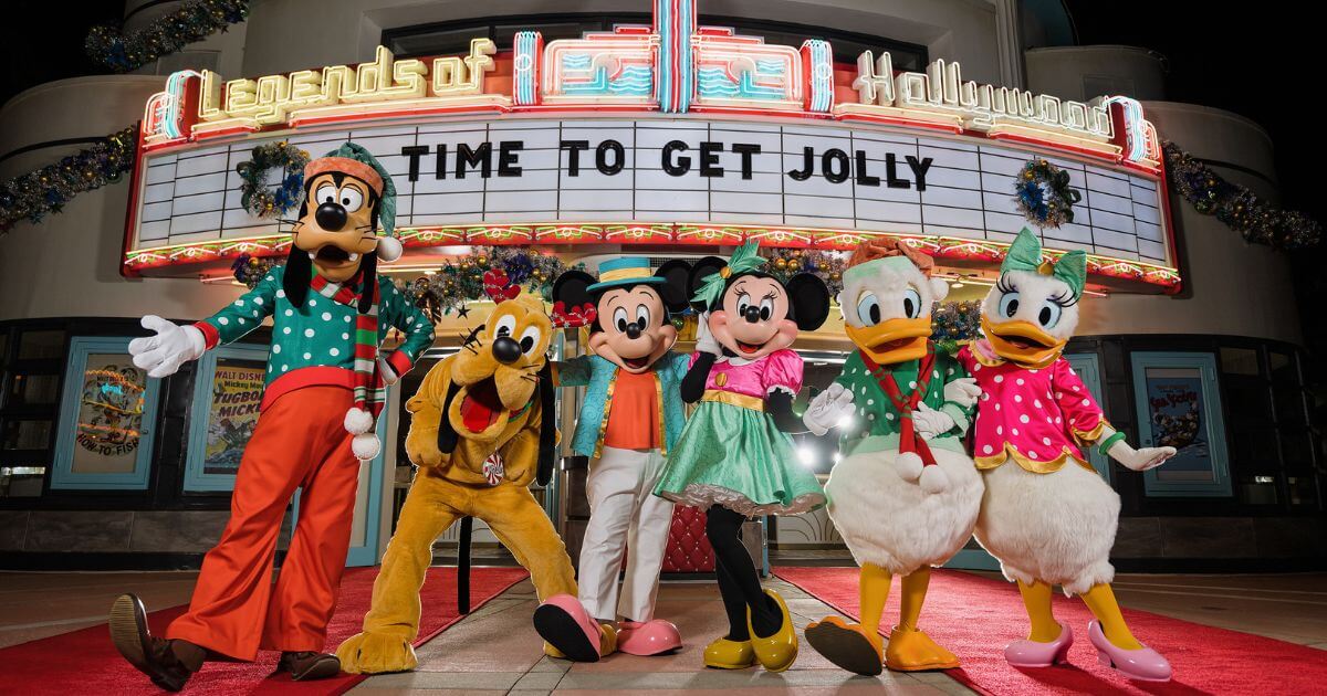 Photo of (L-R) Goofy, Pluto, Mickey, Minnie, Donald, and Daisy in festive holiday attire. A sign behind them on a marquee reads: Time to Get Jolly.