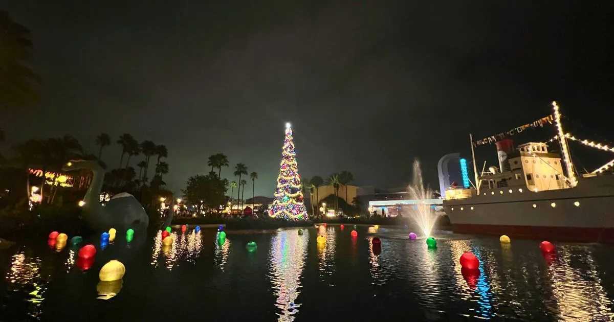 Photo of Echo Lake with Christmas decor - colorful ornaments floating in the water, Santa Gertie, and a huge Christmas tree, all lit up and reflecting off the water of Echo Lake in Hollywood Studios.