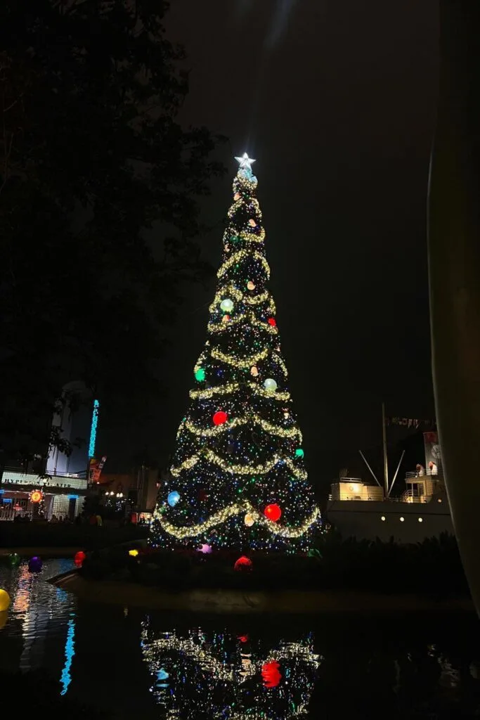 Photo of the Christmas tree lit up at night, reflecting off the water, in Echo Lake at Hollywood Studios.