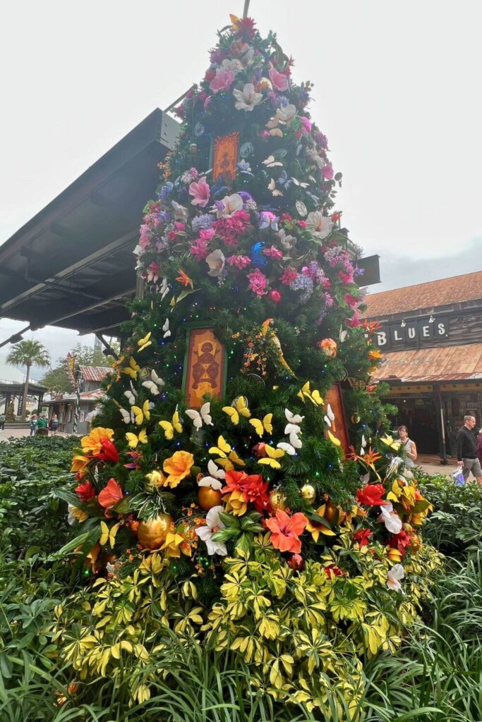Photo of the Encanto Christmas Tree in DIsney Springs with flowers, butterflies, and wood-like character carvings as ornaments.