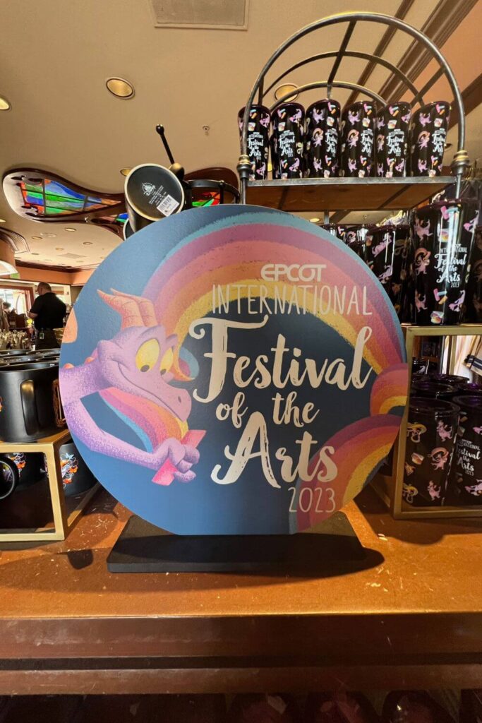 Photo of a store display for Epcot Festival of the Arts merchandise, including tumblers and coffee mugs.