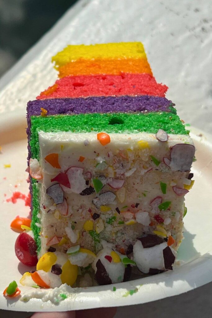 Closeup of a rainbow layered cake with frosting, topped with freeze dried skittles.