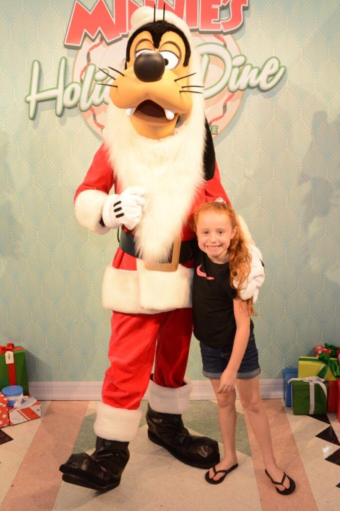 Photo of a young girl posting with Santa Goofy at Minnie's Holiday Dine at Hollywood & Vine restaurant in Disney's Hollywood Studios.