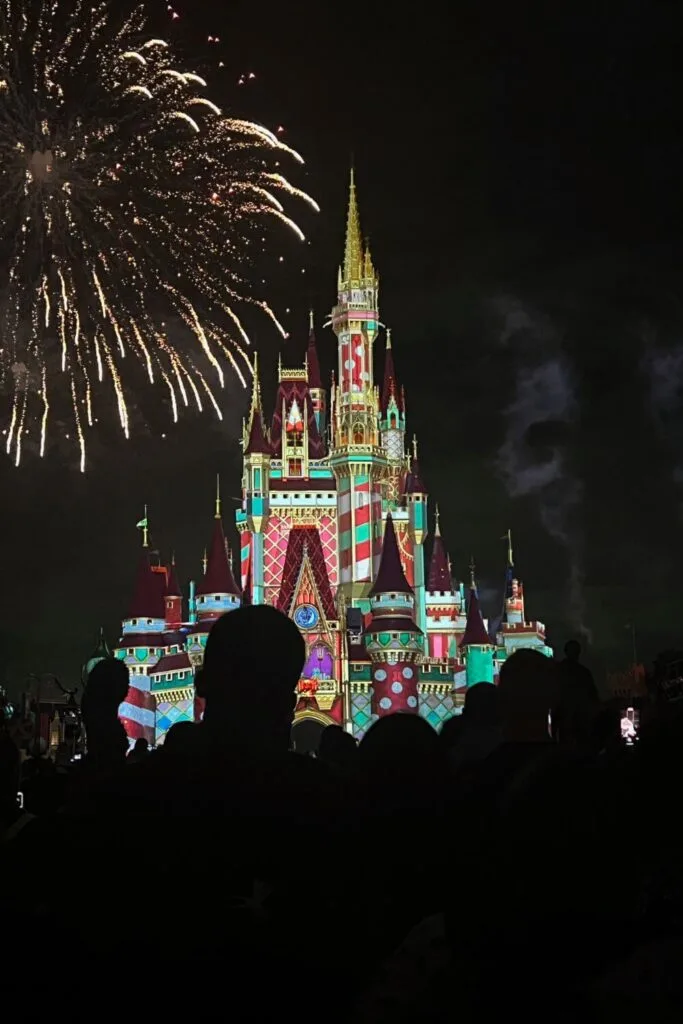 Photo of fireworks exploding over Cinderella Castle while a Christmas themed projection show lights up the castle in red, green, white, and gold.