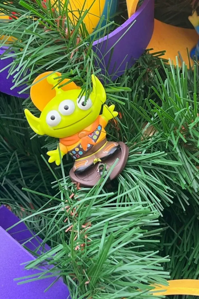Closeup of a Toy Story green alien ornament with an Up Wilderness Explorer uniform.